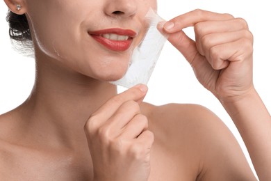 Smiling woman peeling off face mask on white background, closeup