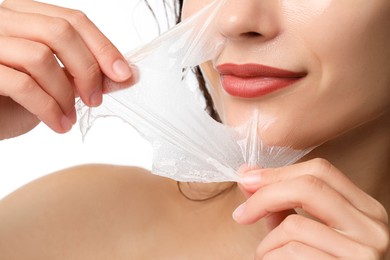 Photo of Woman peeling off face mask on white background, closeup