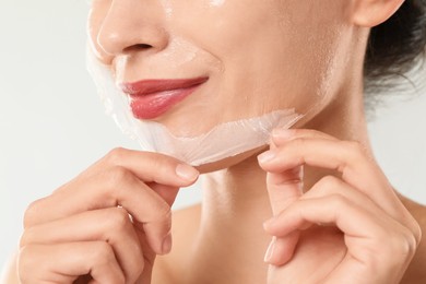 Photo of Woman peeling off face mask on light grey background, closeup