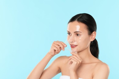 Beautiful woman peeling off face mask on light blue background. Space for text