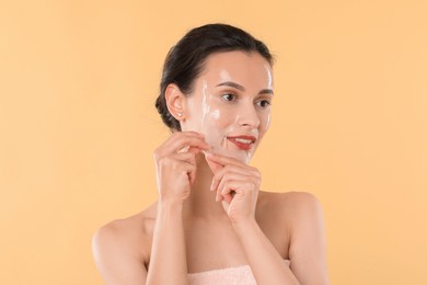 Photo of Smiling woman peeling off face mask on beige background