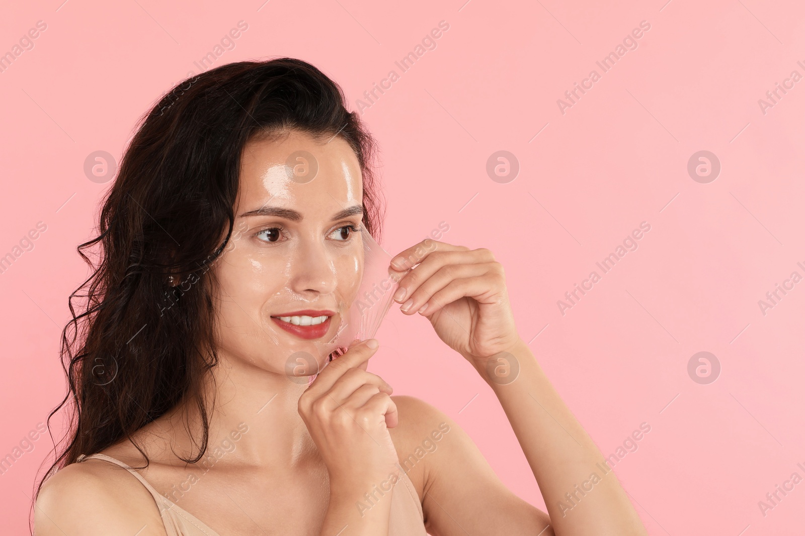 Photo of Smiling woman peeling off face mask on pink background. Space for text