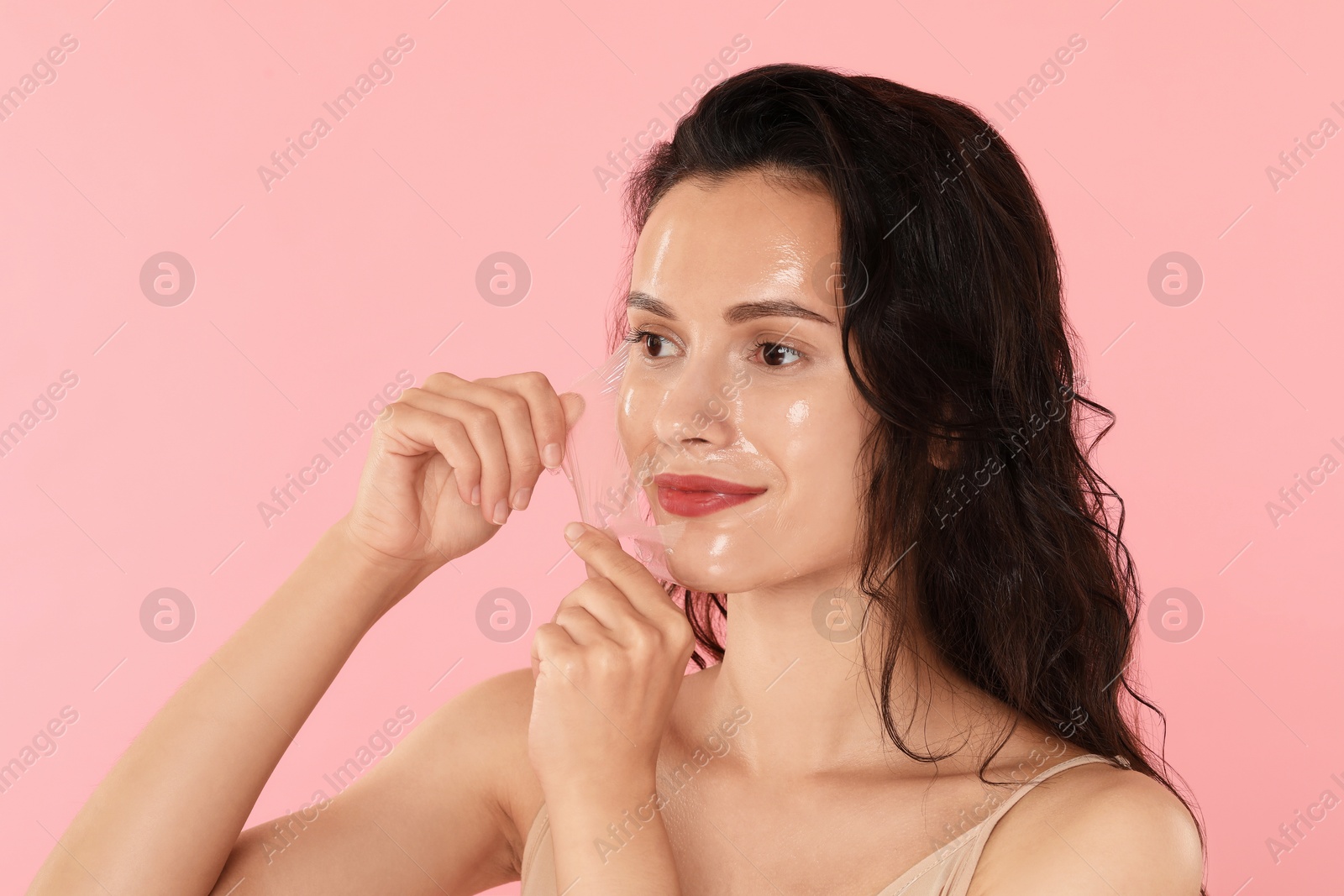 Photo of Beautiful woman peeling off face mask on pink background