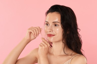 Beautiful woman peeling off face mask on pink background