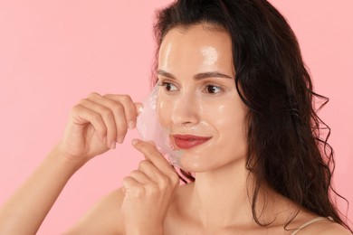 Beautiful woman peeling off face mask on pink background