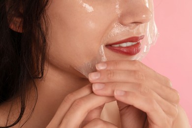 Woman peeling off face mask on pink background, closeup