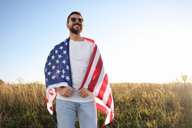 Happy man with flag of USA outdoors, low angle view. Space for text