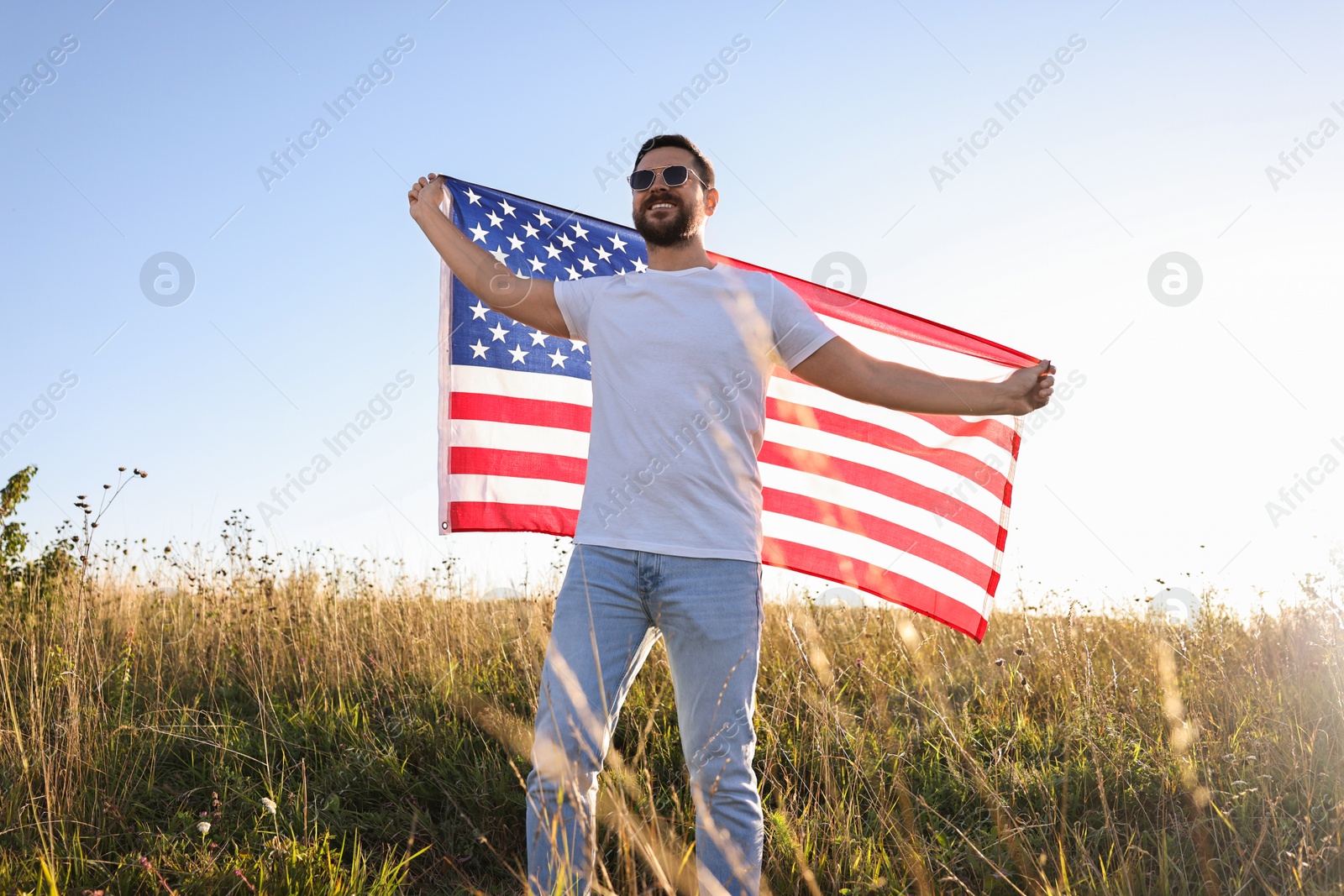 Photo of Happy man with flag of USA outdoors, low angle view