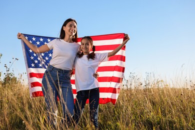 Happy mother and daughter with flag of USA outdoors. Space for text