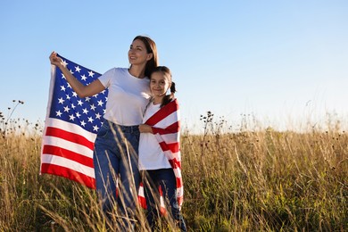 Happy mother and daughter with flag of USA outdoors. Space for text