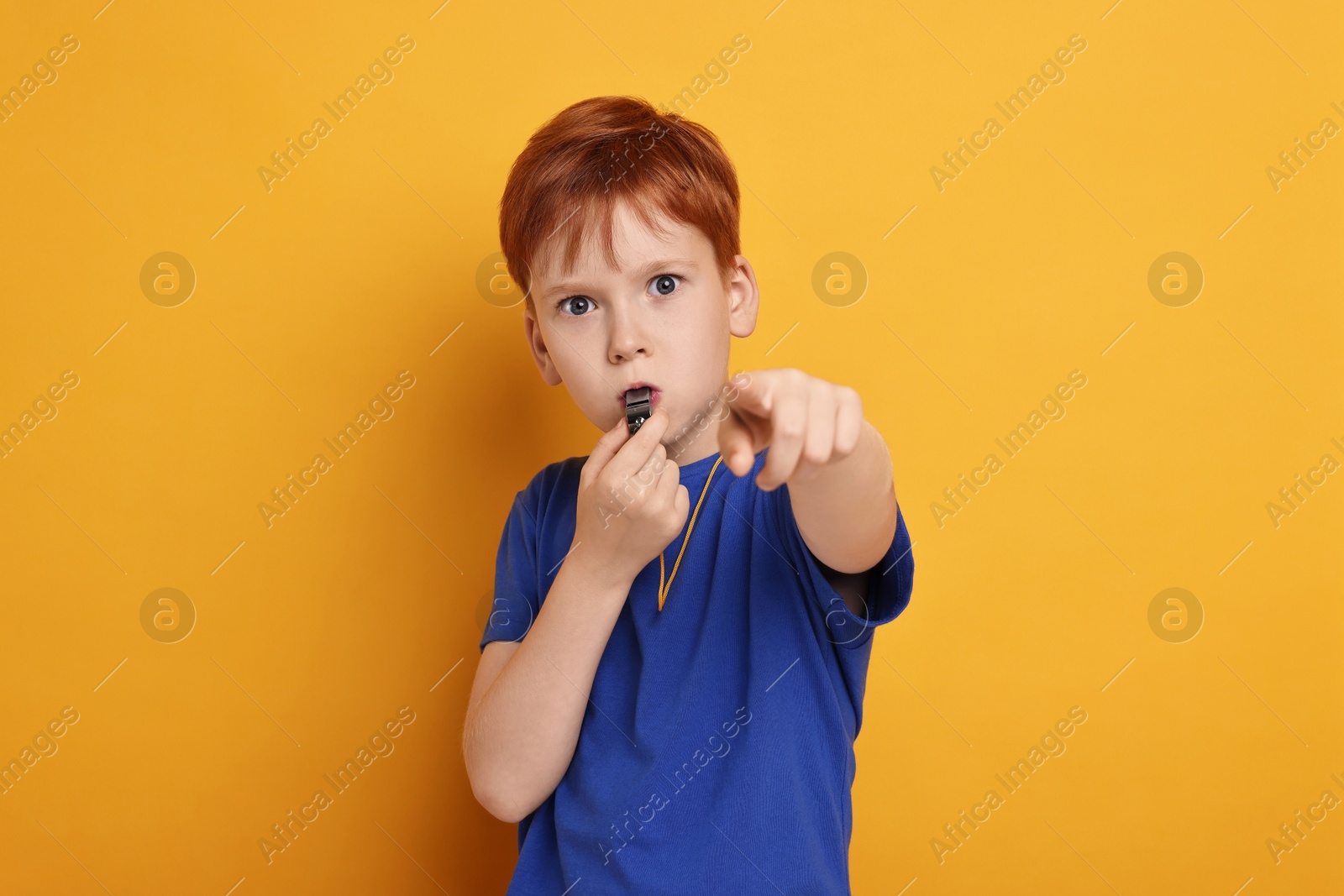 Photo of Little boy blowing whistle on orange background