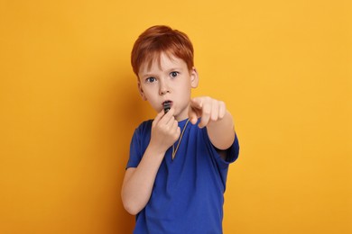 Little boy blowing whistle on orange background