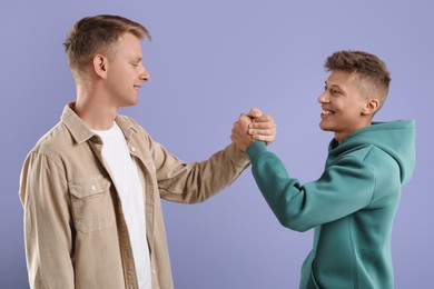 Happy brothers clasping hands on violet background