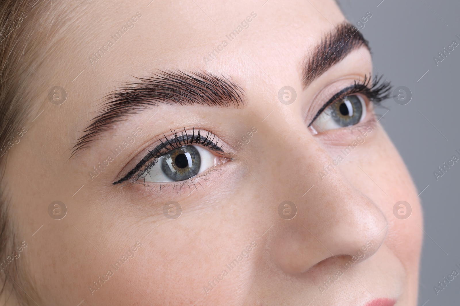 Photo of Woman after brow lamination procedure on grey background, closeup