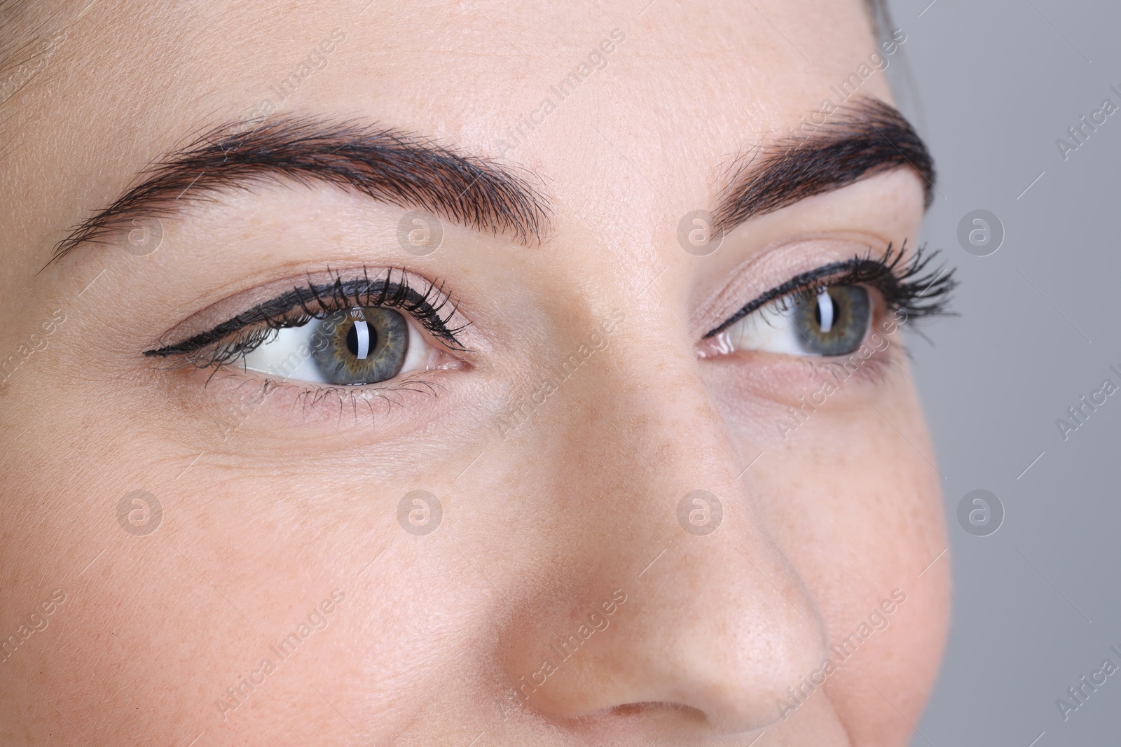 Photo of Woman after brow lamination procedure on grey background, closeup