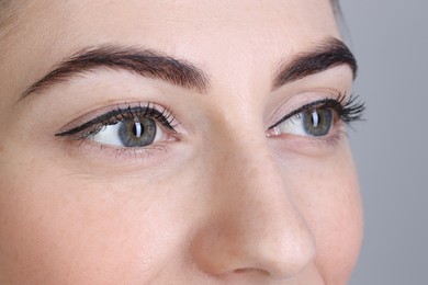 Woman after brow lamination procedure on grey background, closeup