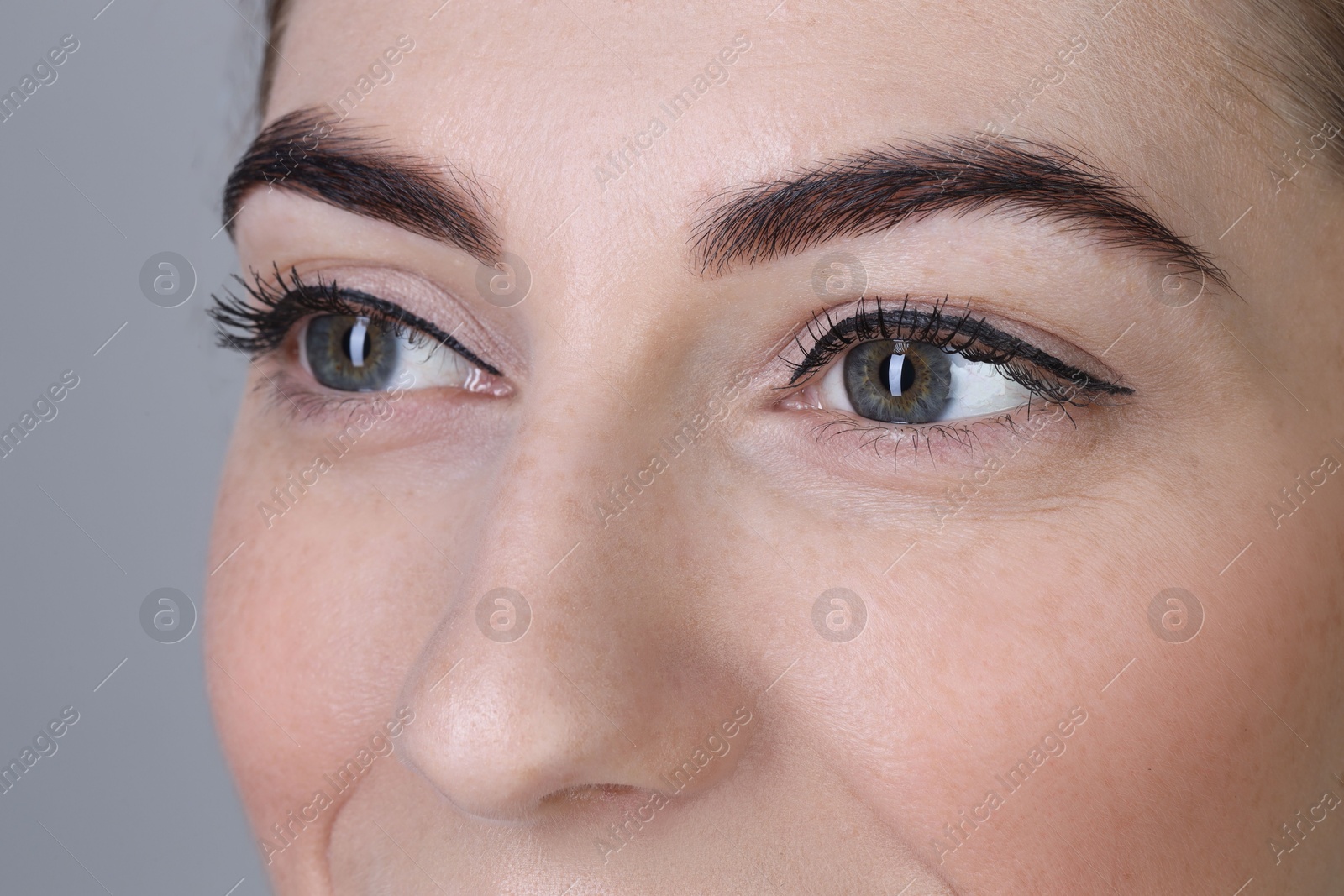 Photo of Woman after brow lamination procedure on grey background, closeup