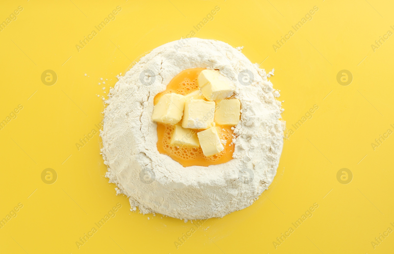 Photo of Cooking homemade pie. Flour with eggs and butter on yellow background, top view