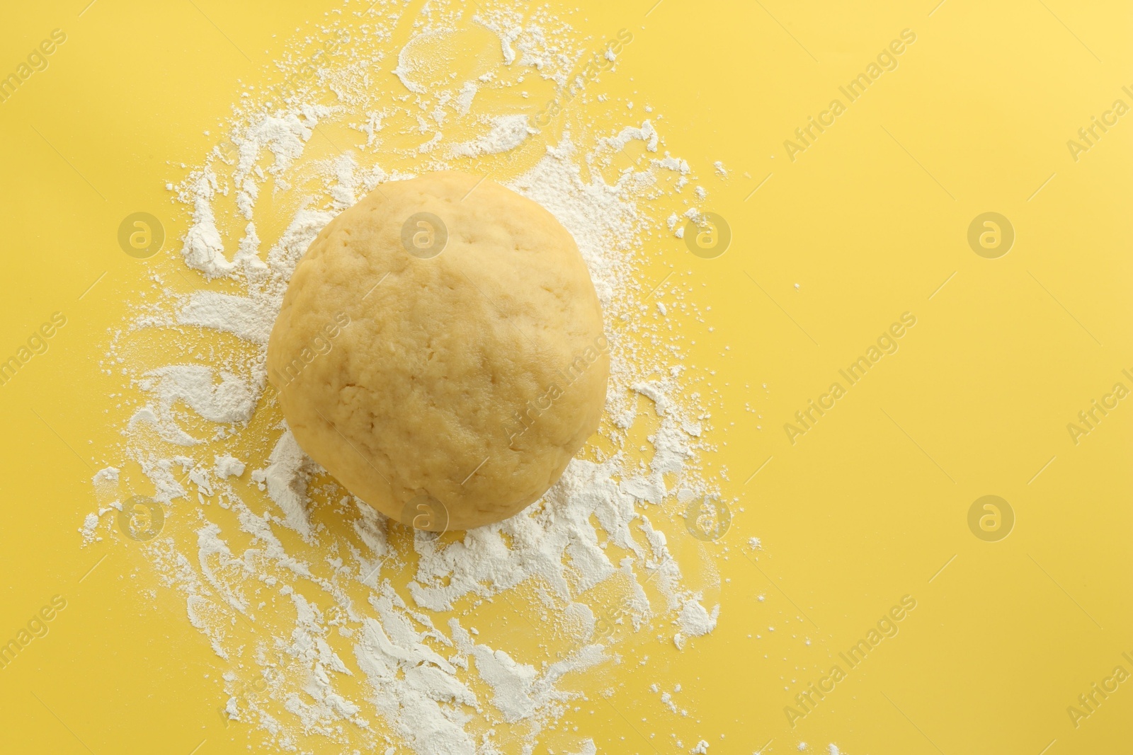 Photo of Cooking homemade pie. Raw dough and flour on yellow background, top view. Space for text