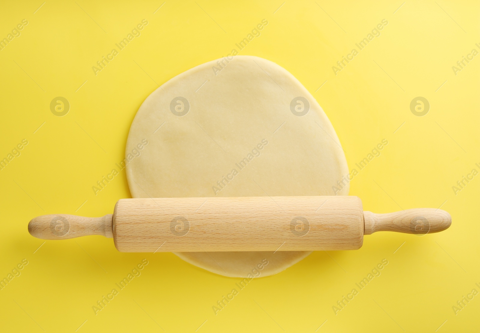 Photo of Cooking homemade pie. Raw dough and wooden rolling pin on yellow background, top view