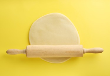 Photo of Cooking homemade pie. Raw dough and wooden rolling pin on yellow background, top view