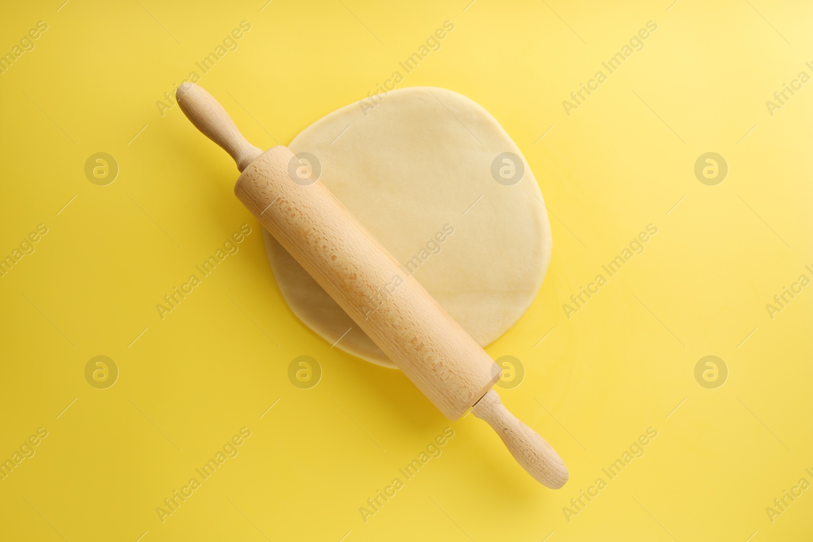 Photo of Cooking homemade pie. Raw dough and wooden rolling pin on yellow background, top view