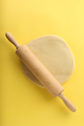 Photo of Cooking homemade pie. Raw dough and wooden rolling pin on yellow background, top view