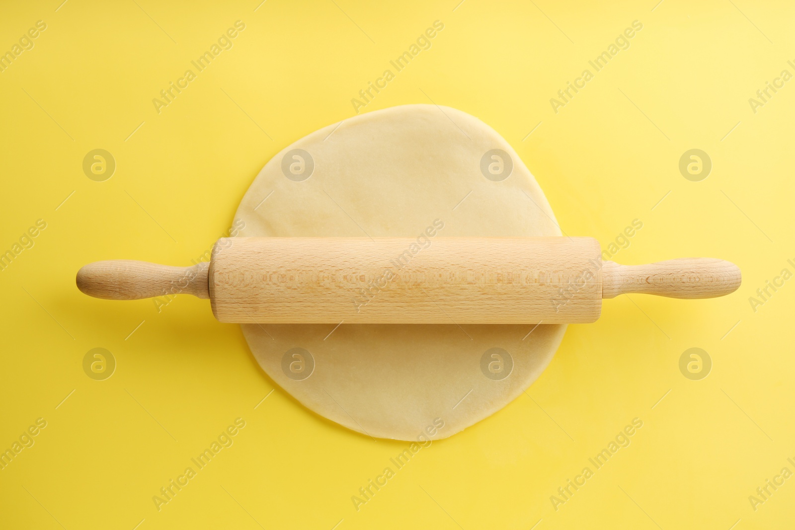 Photo of Cooking homemade pie. Raw dough and wooden rolling pin on yellow background, top view