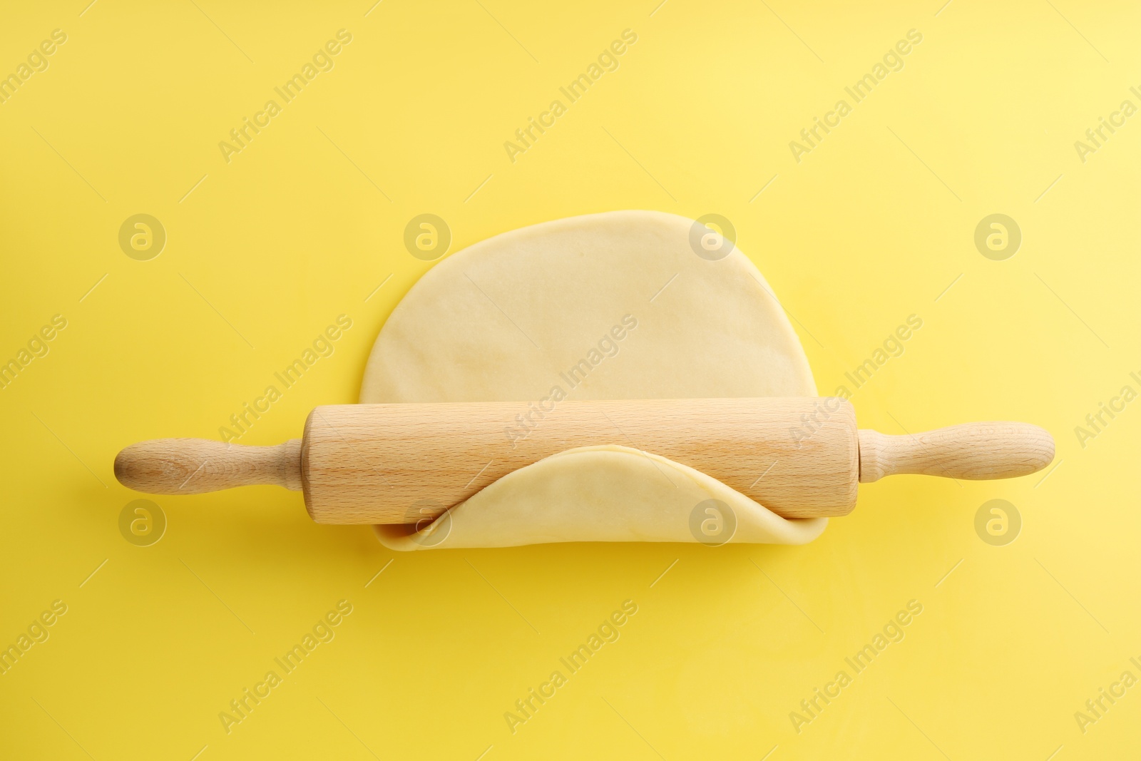 Photo of Cooking homemade pie. Raw dough and wooden rolling pin on yellow background, top view