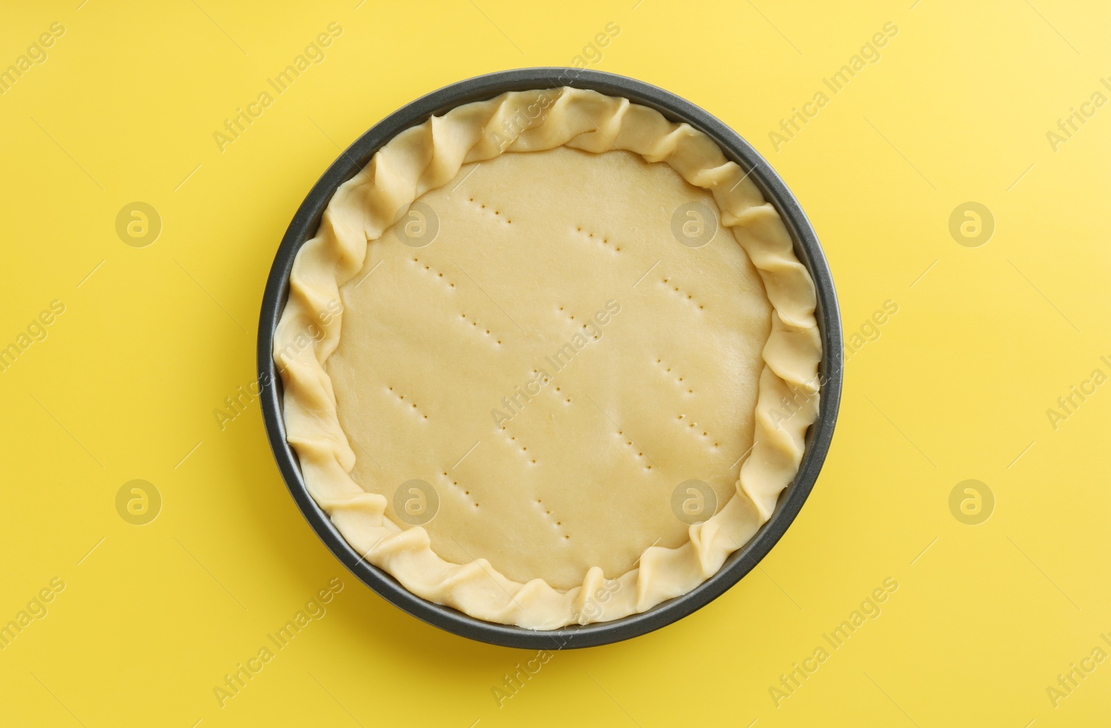 Photo of Cooking homemade pie. Raw dough in baking dish on yellow background, top view