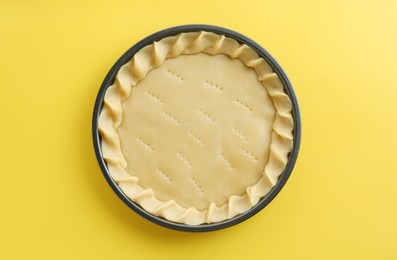 Photo of Cooking homemade pie. Raw dough in baking dish on yellow background, top view