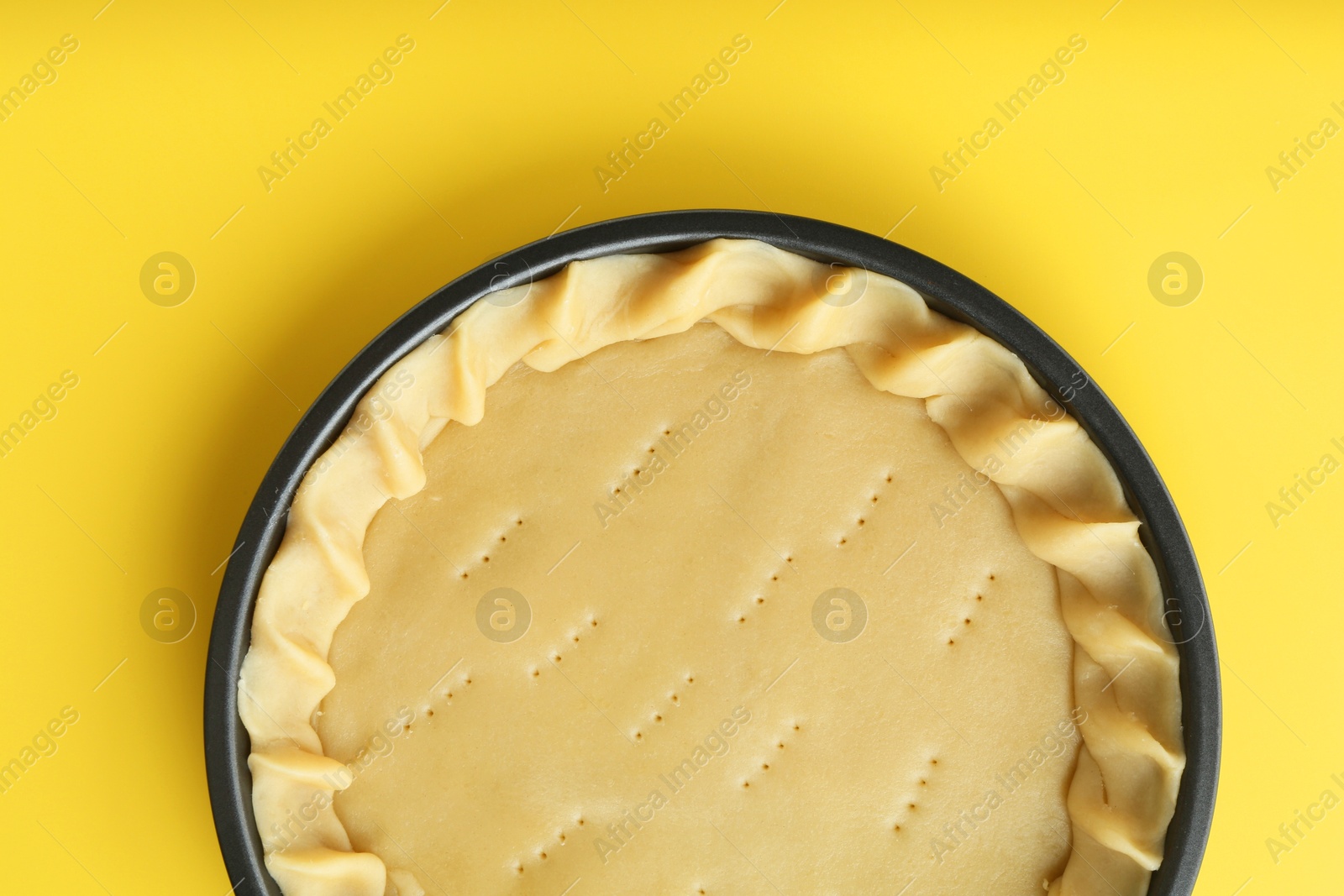 Photo of Cooking homemade pie. Raw dough in baking dish on yellow background, top view