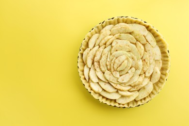 Photo of Raw homemade apple pie on yellow background, top view. Space for text