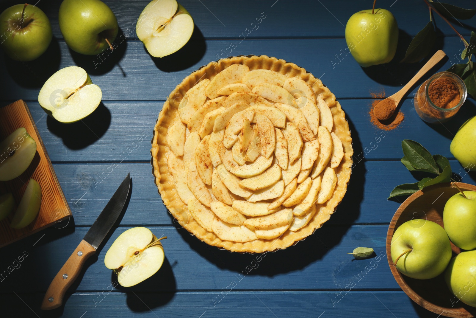 Photo of Uncooked homemade apple pie and ingredients on blue wooden table, flat lay