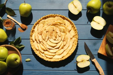 Photo of Uncooked homemade apple pie and ingredients on blue wooden table, flat lay