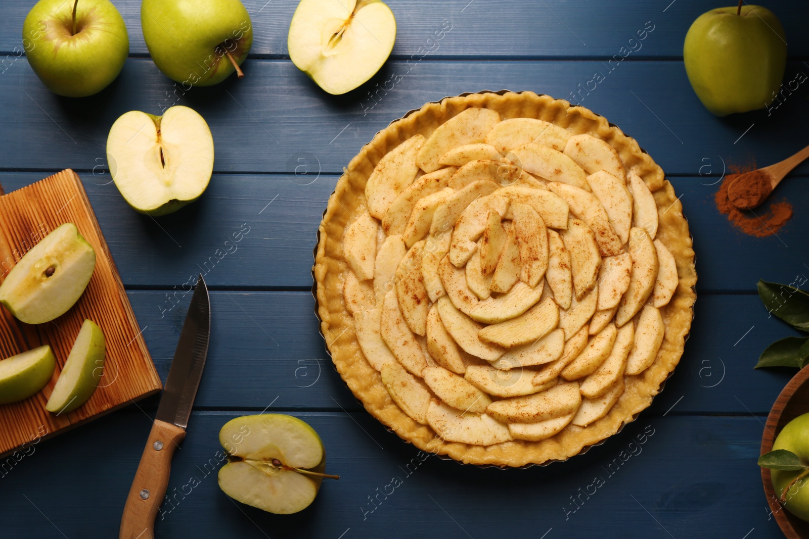 Photo of Uncooked homemade apple pie and ingredients on blue wooden table, flat lay