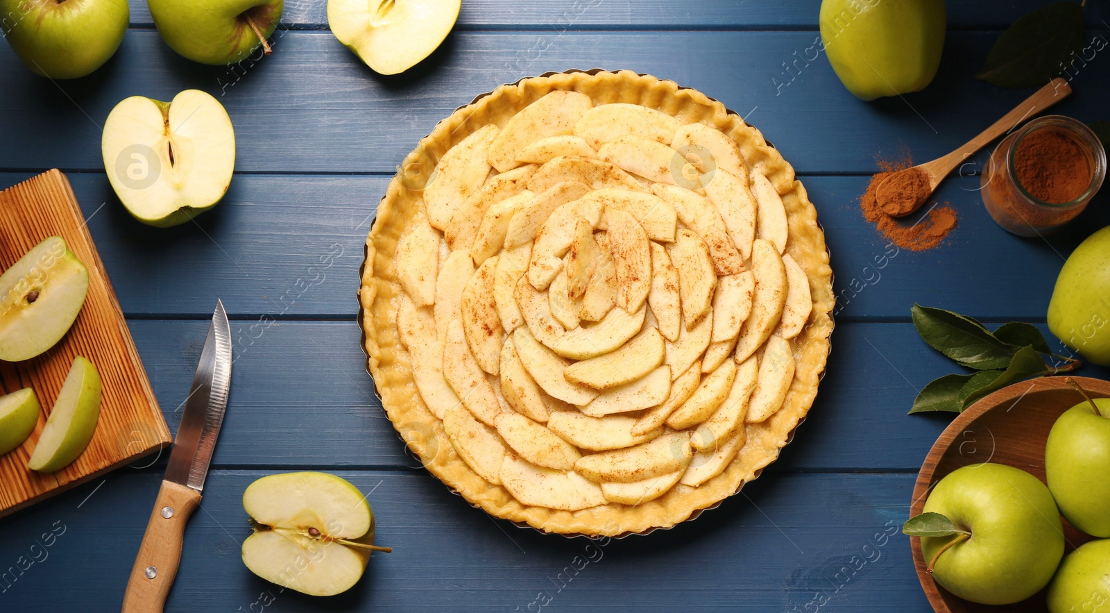 Photo of Uncooked homemade apple pie and ingredients on blue wooden table, flat lay