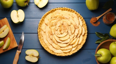 Photo of Uncooked homemade apple pie and ingredients on blue wooden table, flat lay