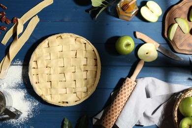 Photo of Uncooked homemade apple pie and ingredients on blue wooden table, flat lay