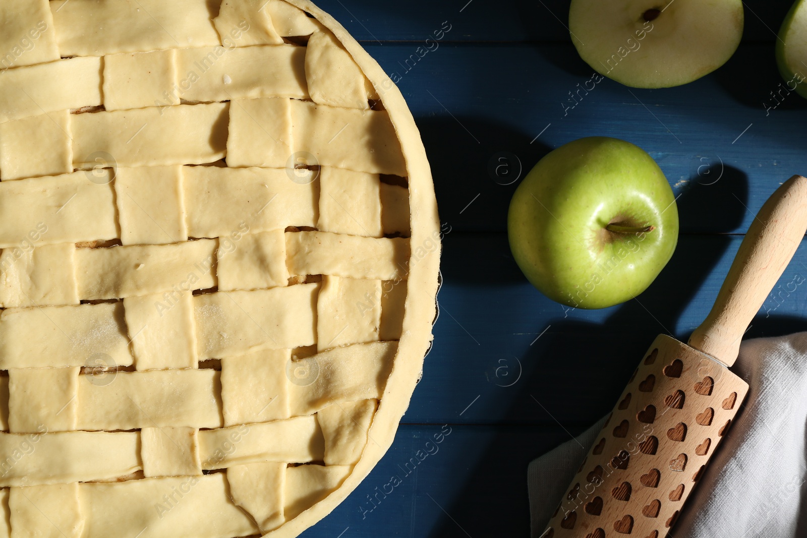 Photo of Uncooked homemade apple pie and ingredients on blue wooden table, flat lay