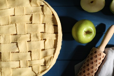 Photo of Uncooked homemade apple pie and ingredients on blue wooden table, flat lay