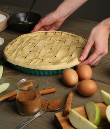 Photo of Woman making homemade apple pie and ingredients on wooden table, closeup