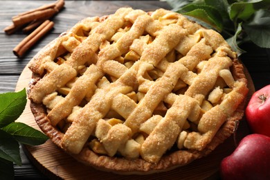 Photo of Tasty homemade apple pie and ingredients on wooden table, closeup