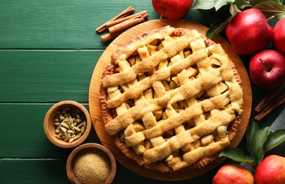 Tasty homemade apple pie and ingredients on green wooden table, flat lay