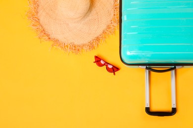 Photo of Turquoise suitcase, straw hat and sunglasses on yellow background, flat lay. Space for text