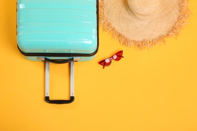 Photo of Turquoise suitcase, straw hat and sunglasses on yellow background, flat lay. Space for text