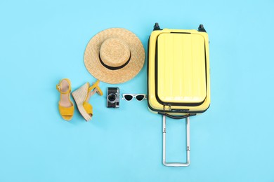 Photo of Yellow suitcase, shoes, sunglasses, wicker hat and camera on light blue background, flat lay