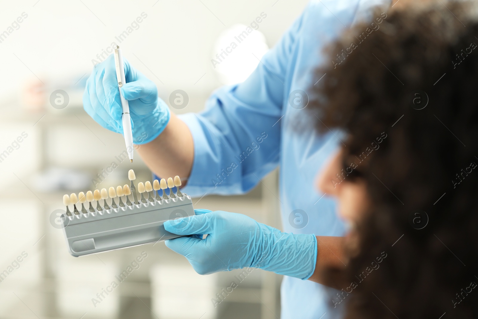 Photo of Doctor and patient choosing shade on teeth color palette in clinic, closeup. Dental veneers