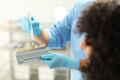 Doctor and patient choosing shade on teeth color palette in clinic, closeup. Dental veneers