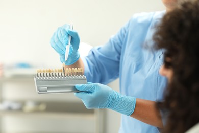 Doctor and patient choosing shade on teeth color palette in clinic, closeup. Dental veneers